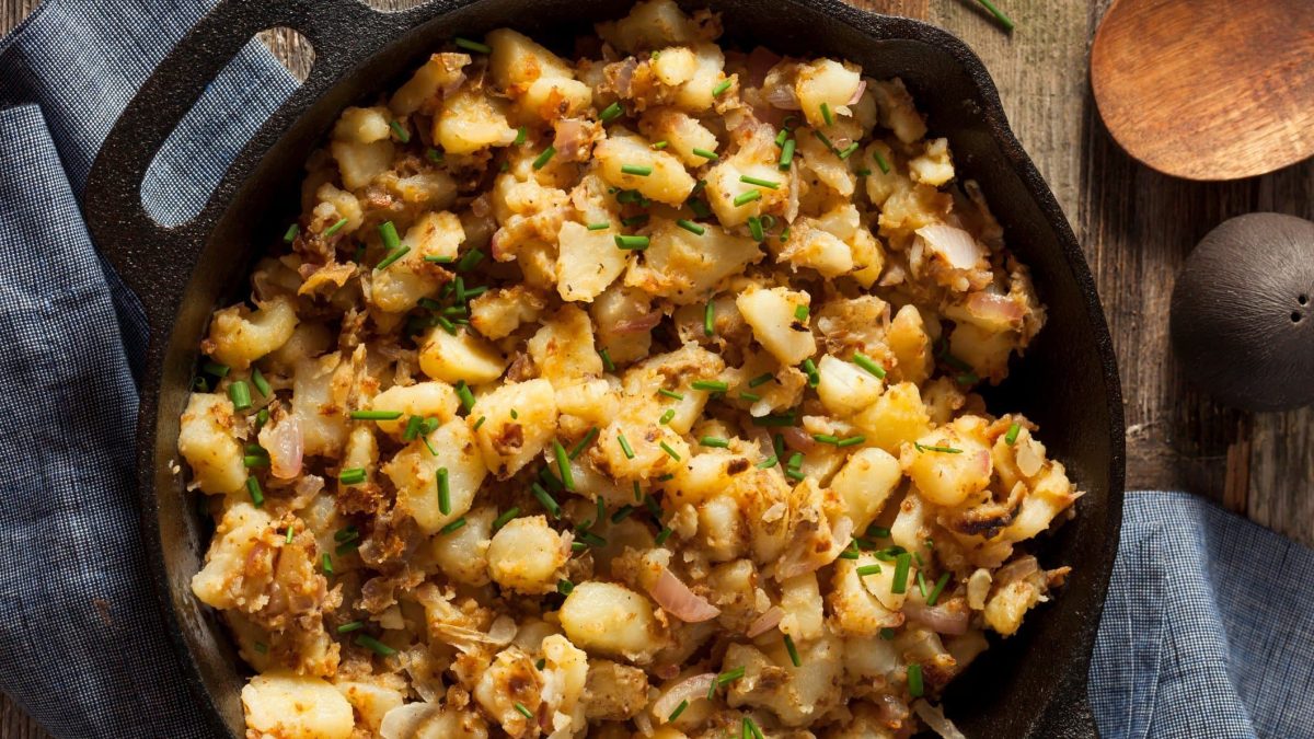 Kartoffelsterz mit Zwiebeln und Schnittlauch in gusseiserner Pfanne.