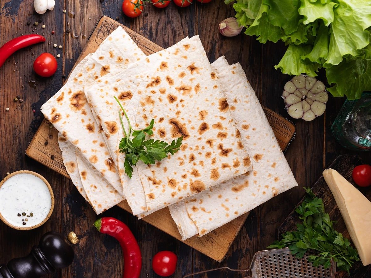 Ein Holzbrett mit Lavash darauf neben frischen Zutaten.