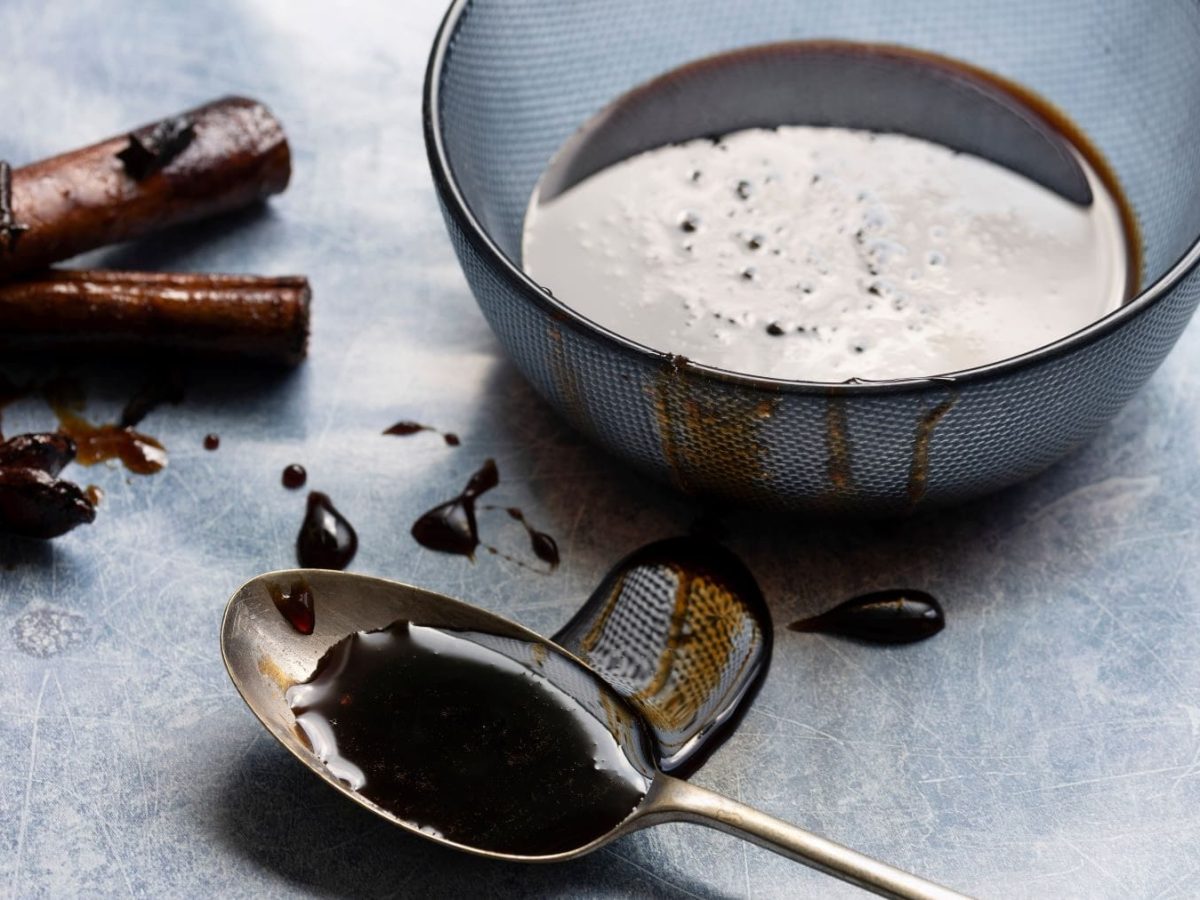 Masala Chai Sirup in blauer Schale auf grauem Untergrund. Im Bild ein Teelöffel, von dem Sirup herunter läuft. Oben Zimt und Sternanis. Draufsicht.