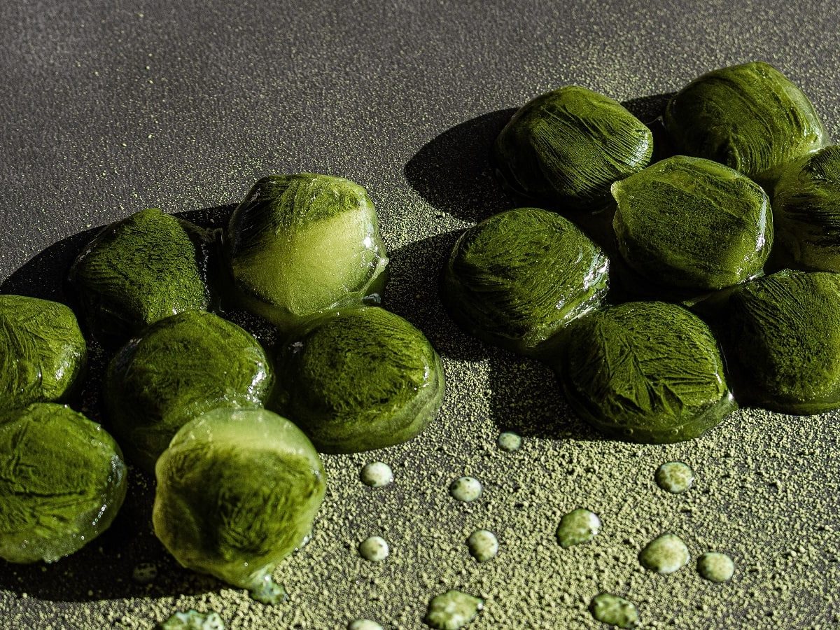 Einige Matcha-Eiswürfel auf einem grauen Untergrund.