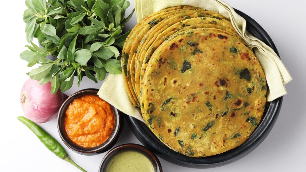 Ein schwarzer Teller mit Methi Paratha neben frischen Zutaten.