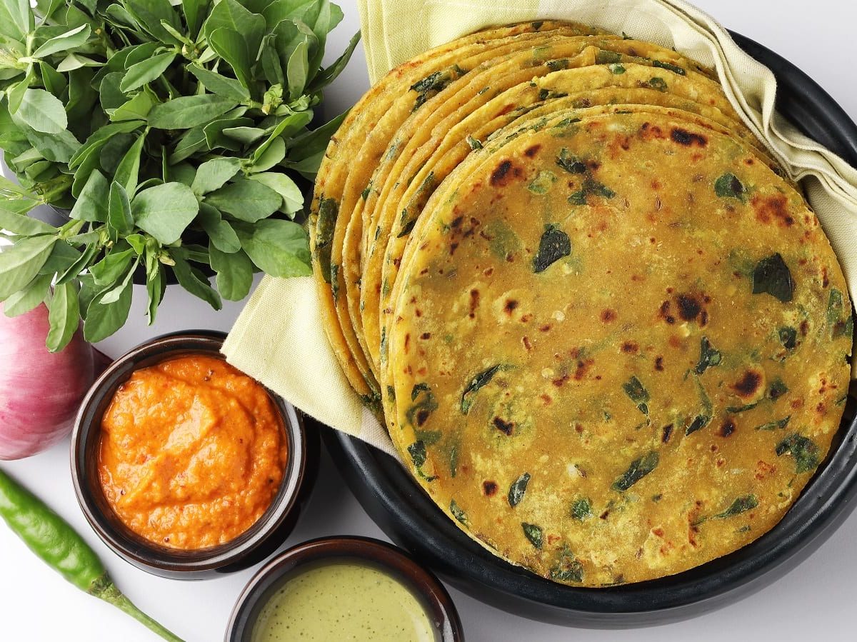 Ein schwarzer Teller mit Methi Paratha neben frischen Zutaten.