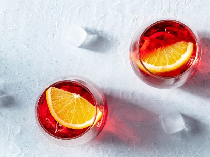 Zwei Gläser Negroni Spritz auf einem weißen Tisch.