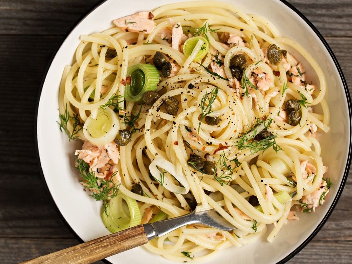 Ein Teller mit Zitronenbutter-Pasta mit Lachs auf einem Holztisch.