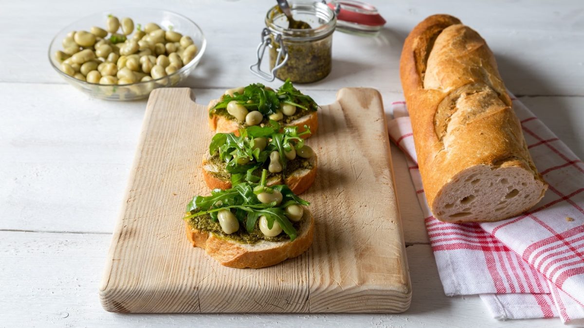 Ein Holzbrett mit drei Brotstücken mit Pesto di fave darauf.