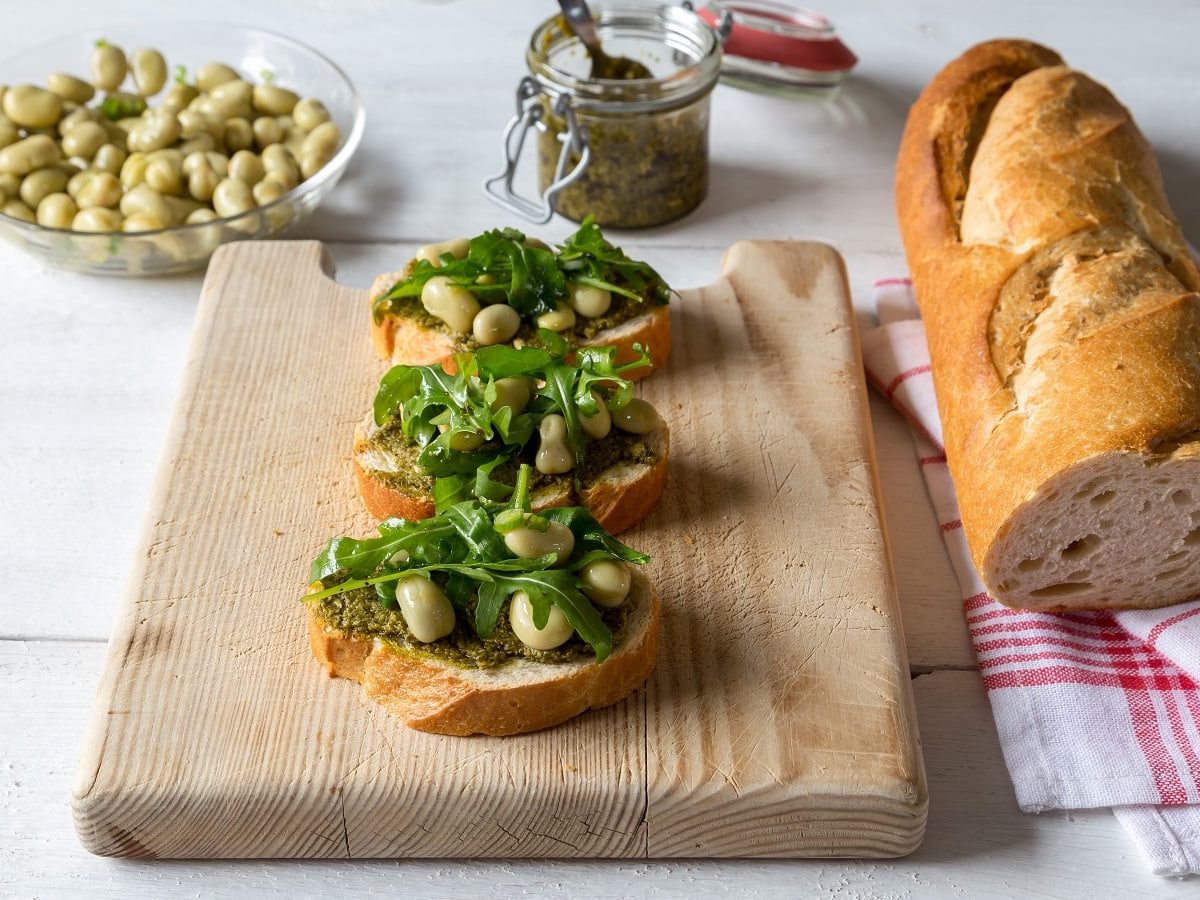 Ein Holzbrett mit drei Brotstücken mit Pesto di fave darauf.