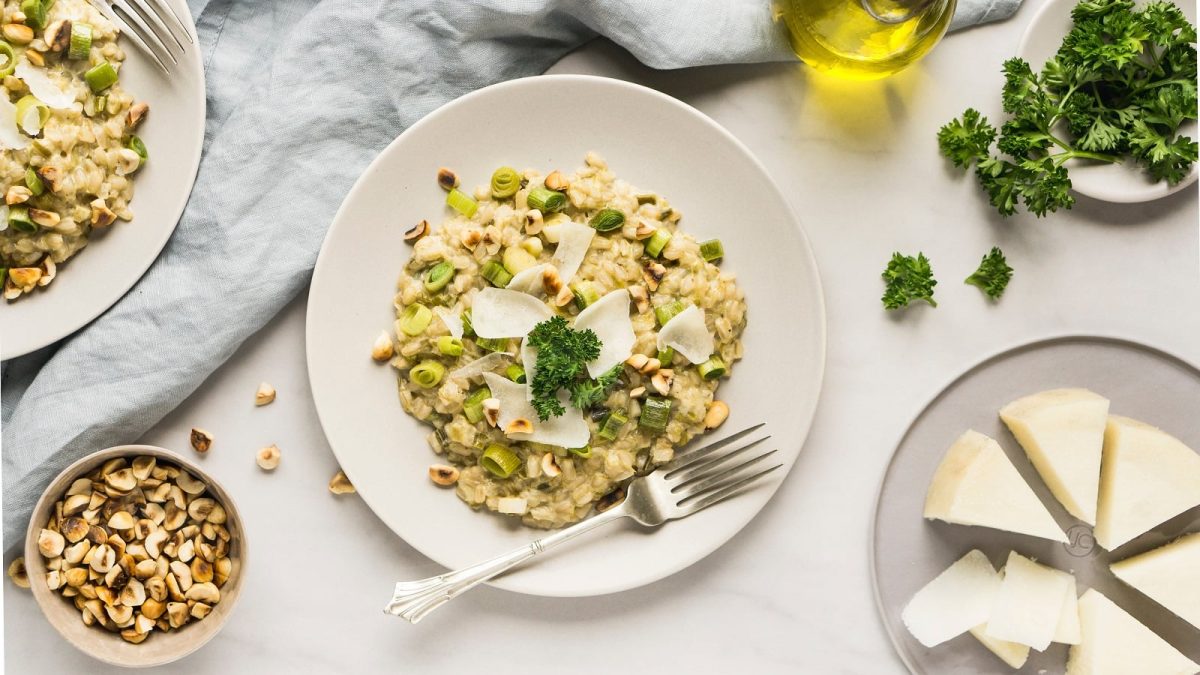 Ein weißer runder Teller mit Porree-Risotto neben frischen Zutaten.