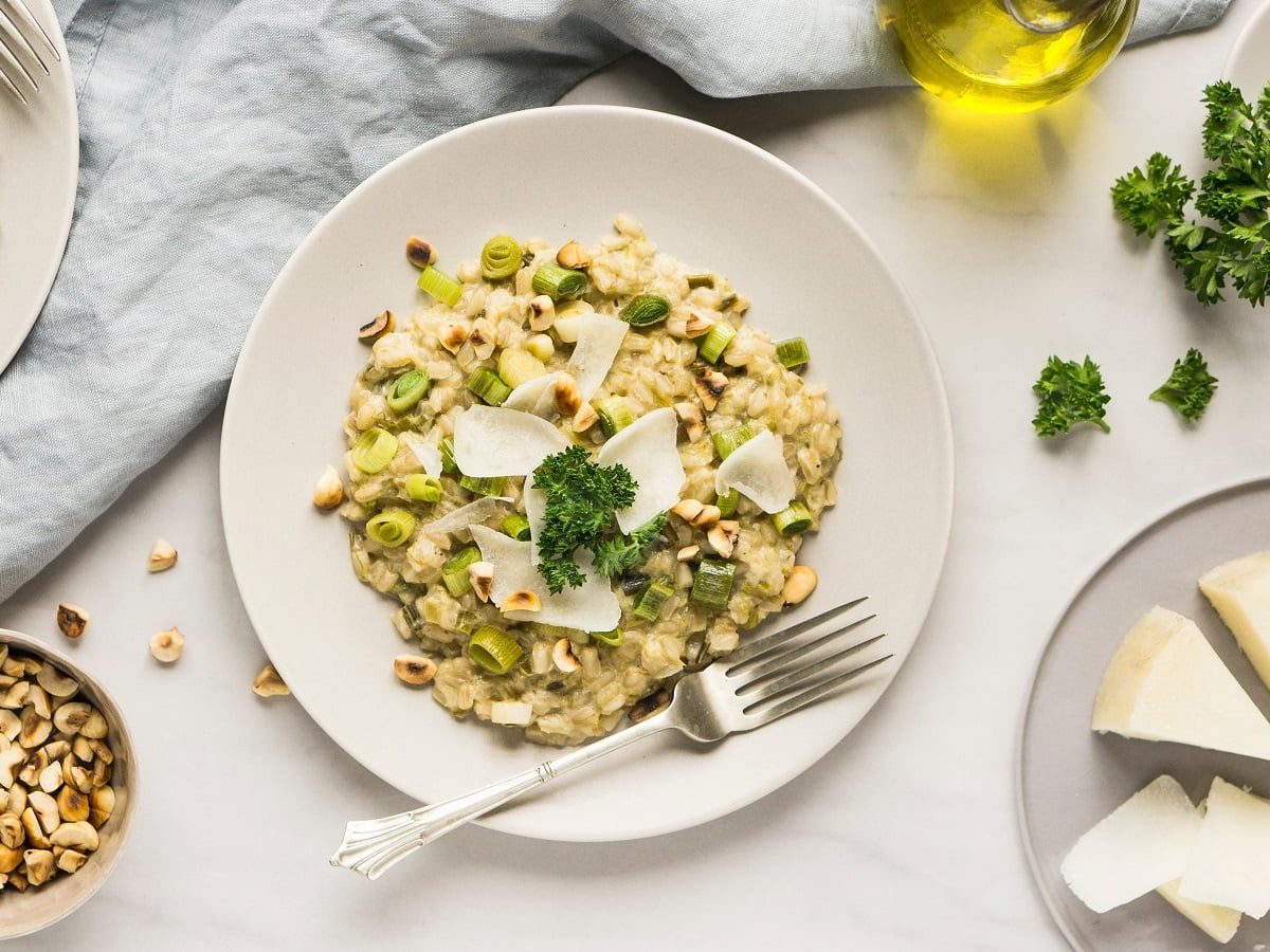 Ein weißer runder Teller mit Porree-Risotto neben frischen Zutaten.