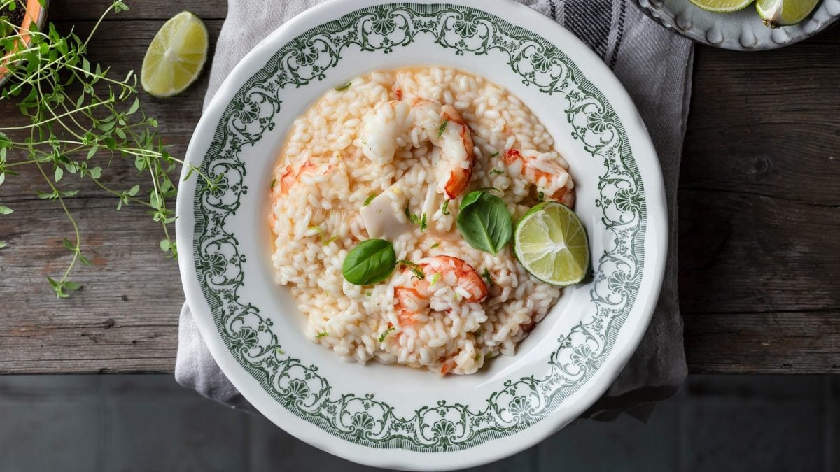 Ein Teller mit grünem Rand und dem Risotto mit Shrimps auf einem rustikalen Holztisch.