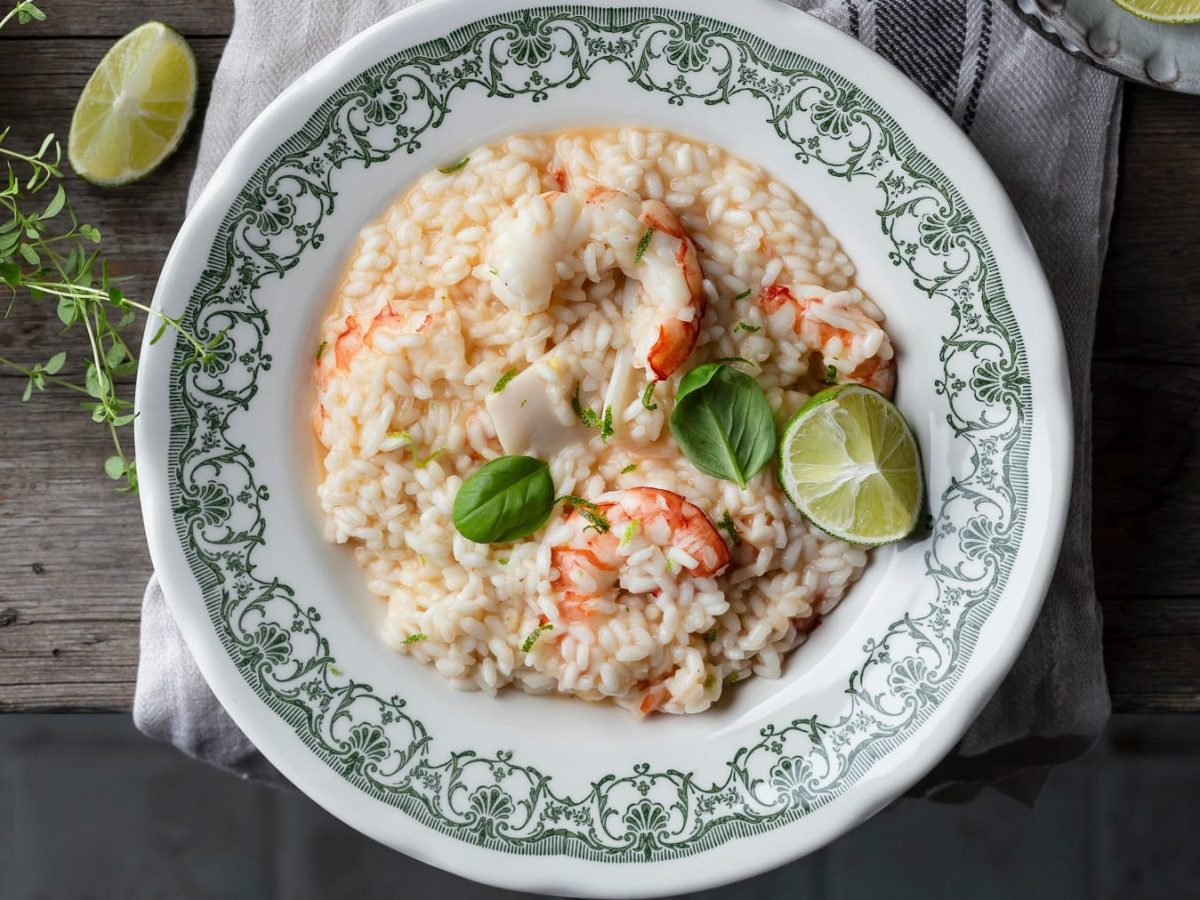 Ein Teller mit grünem Rand und dem Risotto mit Shrimps auf einem rustikalen Holztisch.