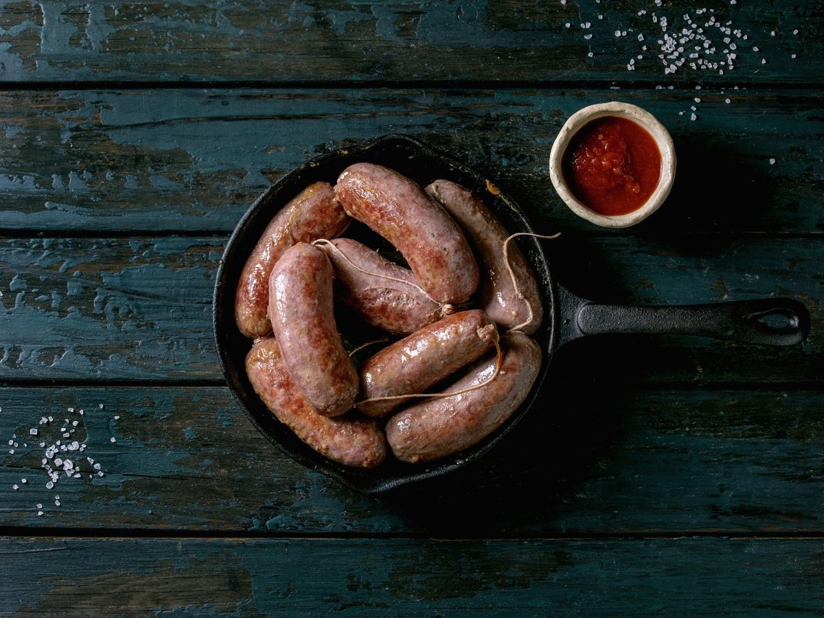 Draufsicht: Dunkler Untergrund, eine Schüssel mit mehreren Salsiccia, also Bratwürsten. Daneben eine Schälchen mit Ketchup.