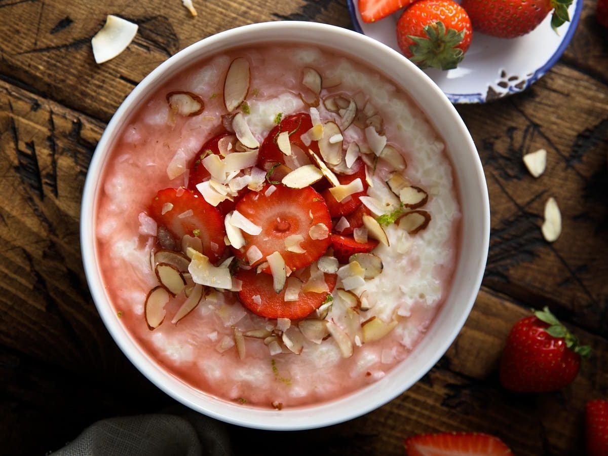 Eine weiße Schüssel mit Rhabarber-Erdbeer-Porridge auf einem dunklen Holztisch.