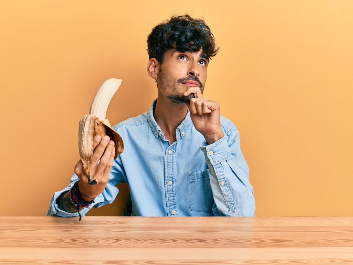 Sind Bananen vegan: Ein junger Mann mit nachdenklichem Blick hält eine geschälte Banane in der Hand.