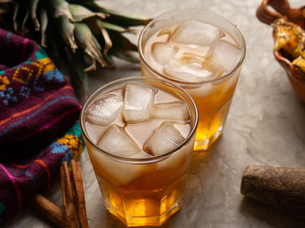 Selbst gemachte Tepache Mexikanische fermentierte Ananas-Limonade in zwei Gläsern mit Zutaten und buntem Stoff im Bild auf hellem Unterrgund. Draufsicht.