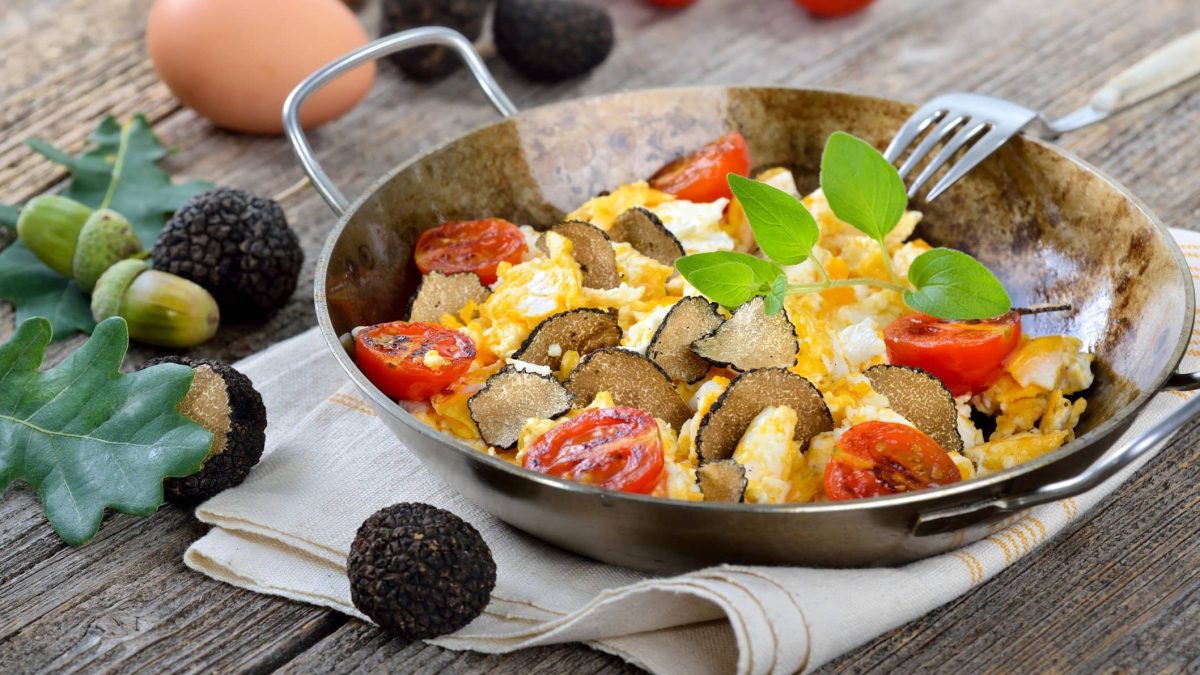 Feines Rührei mit Trüffel und Tomaten in Pfanne auf Holztisch.