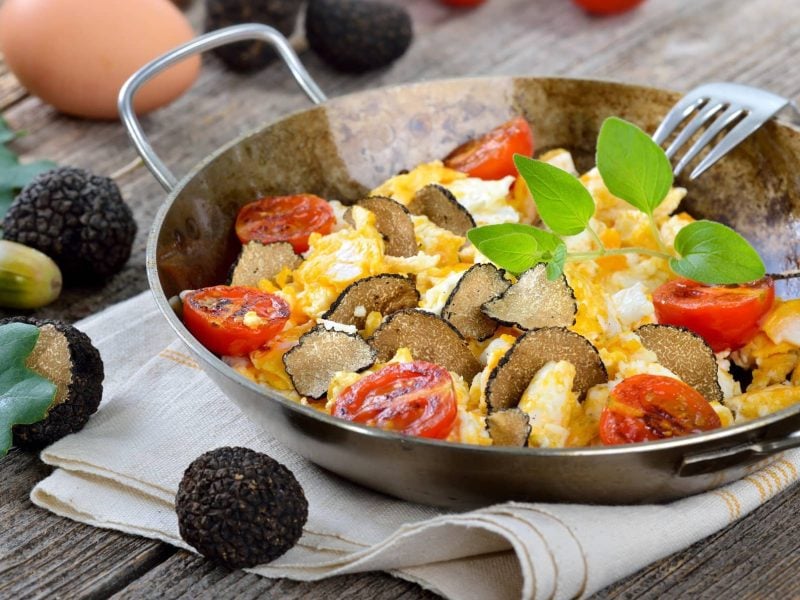 Feines Rührei mit Trüffel und Tomaten in Pfanne auf Holztisch.