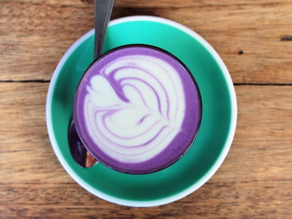 Eine türkise Untertasse mit Ube Latte auf einem hellen Holztisch