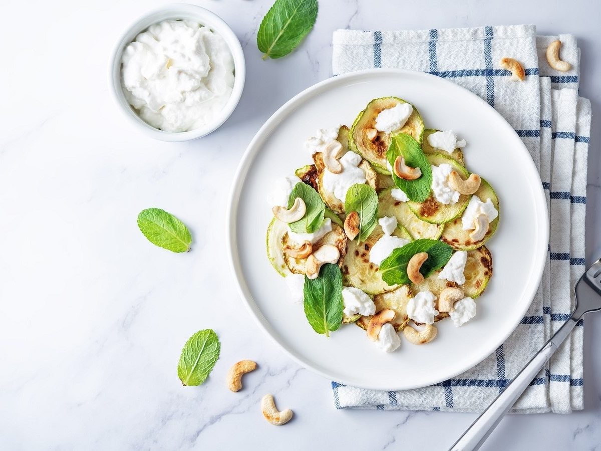 Ein weißer Teller mit Zucchini-Salat mit Ricotta auf einem Küchentuch.