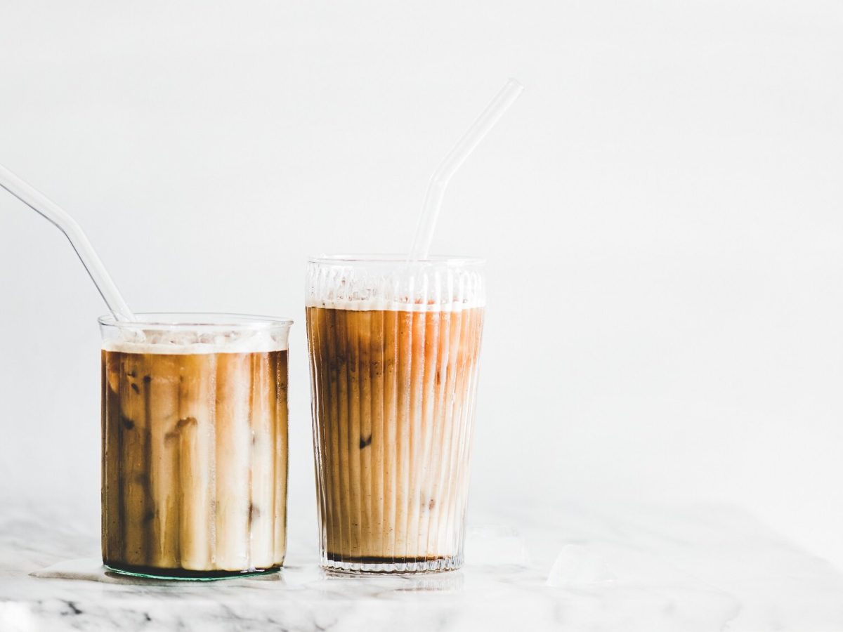 Zwei Gläser Iced Banana Latte mit Strohhalm und Eis auf einem Marmortisch.