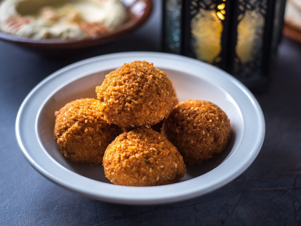 Fünf frittierte Blumenkohlbällchen in einer weißen Schale. Im Hintergrund ein orientalisches Licht und eine Schale mit dem Joghurt-Dip.