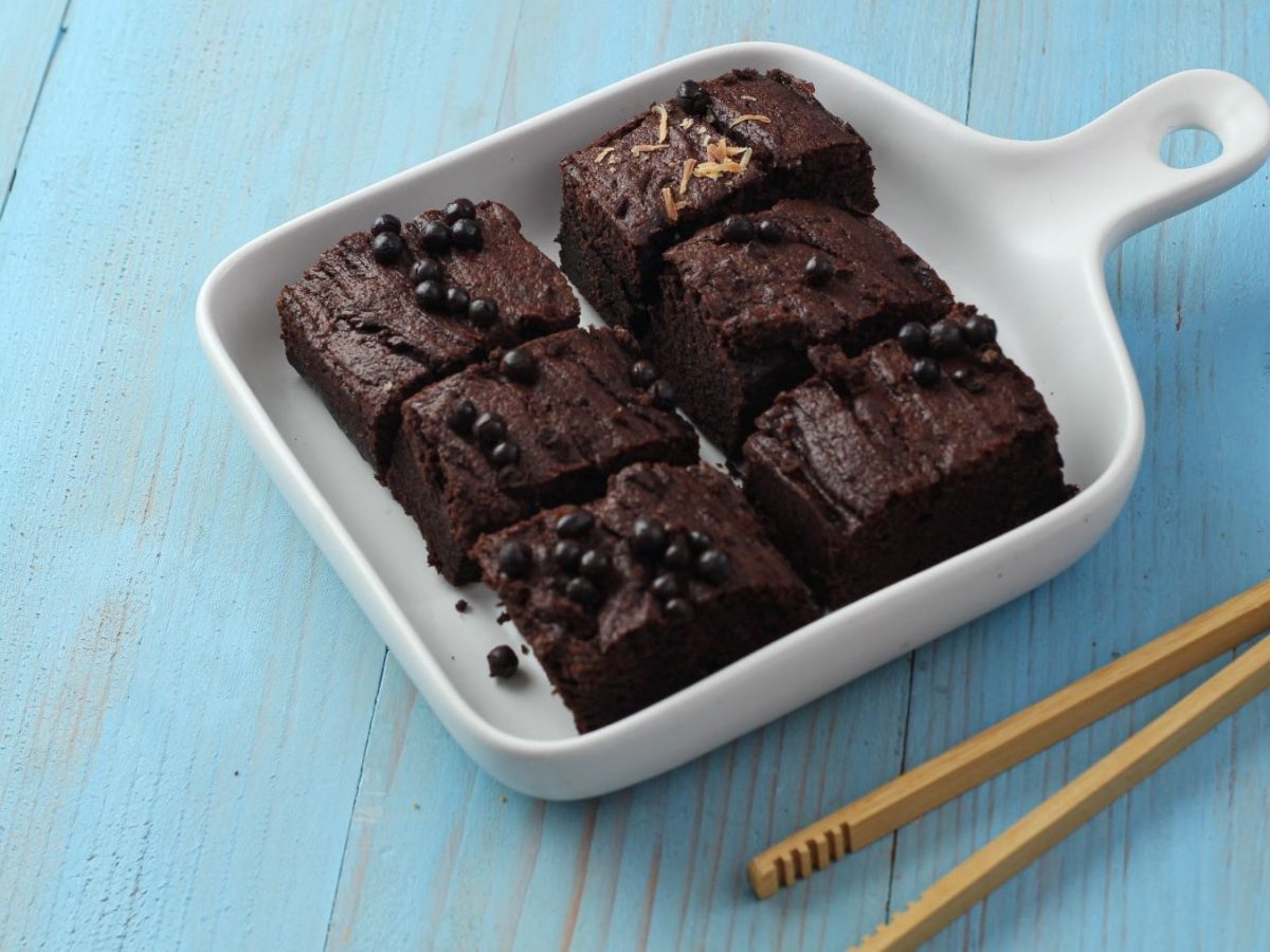 Breakfast Brownie in 2 Minuten aus der Mikrowelle in weißer Form auf blauem Tisch. Daneben Zange aus Holz. Draufsicht..