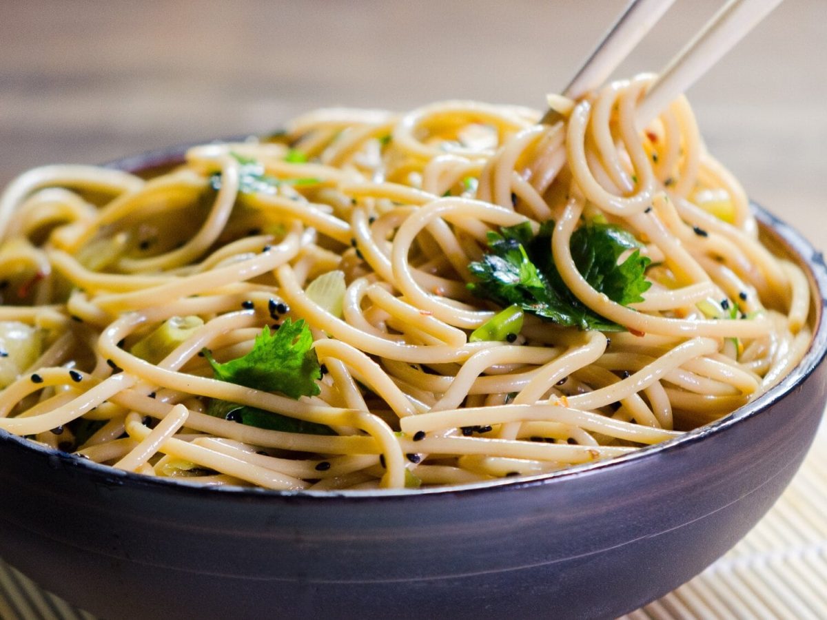 Eine Schüssel Cashew-Sesam-Pasta mit Kräutern, darin Essstäbchen.