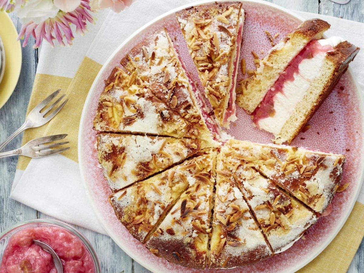 Auf einem Teller ist ein gefüllter Rhabarber-Butterkuchen angerichtet. Er ist mit Mandeln verfeinert.