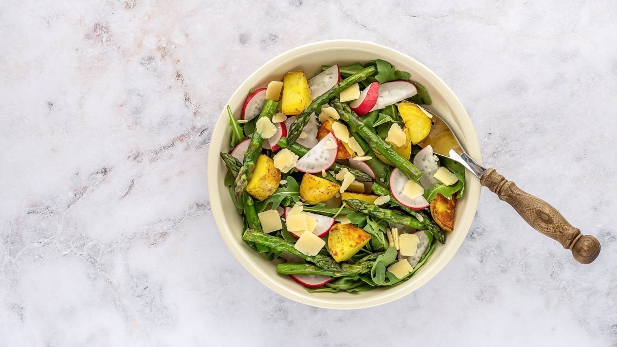 Eine Schüssel gegrillter Spargel-Kartoffel-Salat mit Radieschen und Rucola, darin eine Gabel, in der Draufsicht.