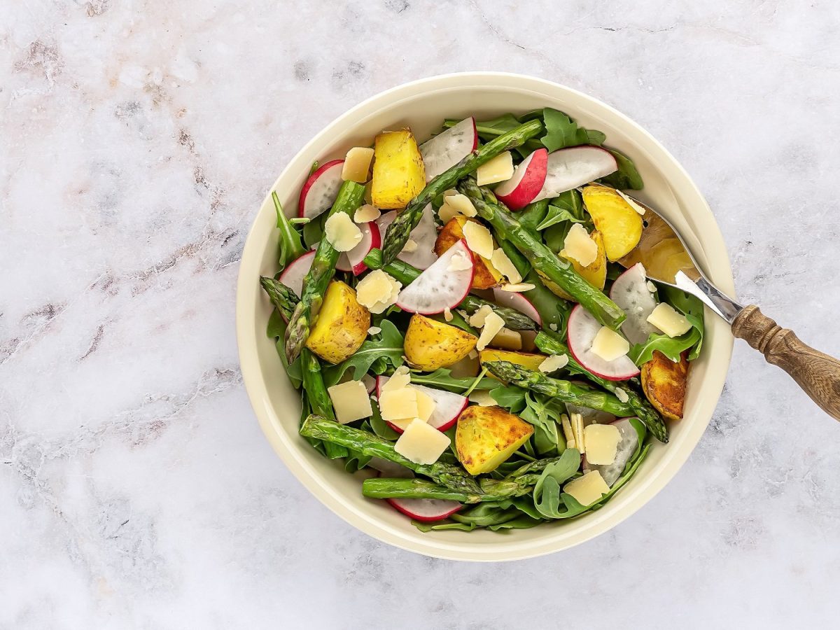 Eine Schüssel gegrillter Spargel-Kartoffel-Salat mit Radieschen und Rucola, darin eine Gabel, in der Draufsicht.