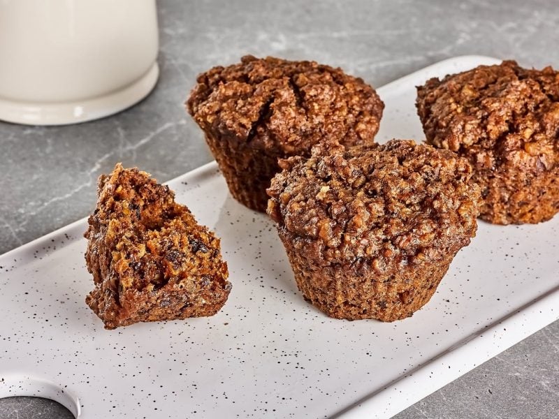 Ein weißes Brett mit den Granola-Muffins auf einem grauen Steintisch. Im Hintergrund weiße Keramik erkennbar.