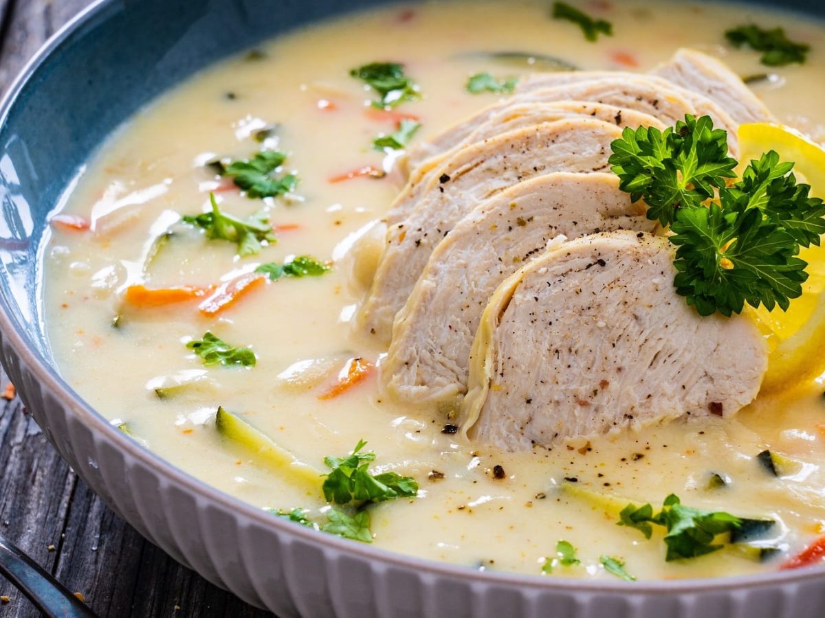 Eine tiefe Schale mit griechischer Zitronen-Cremesuppe auf einem dunklen Tisch.