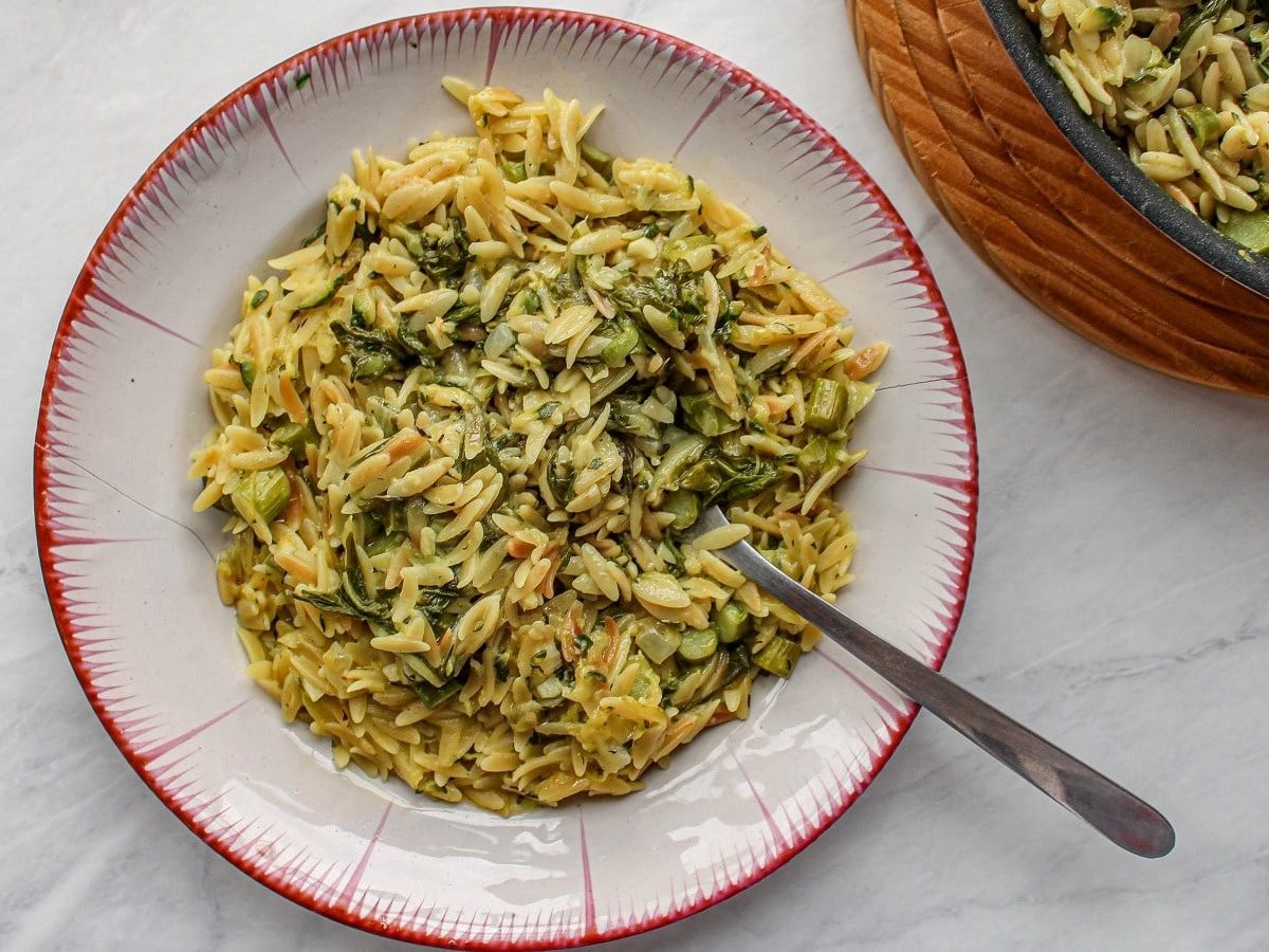 Ein weißer Teller mit Orzo Primavera auf einem hellen Tisch.