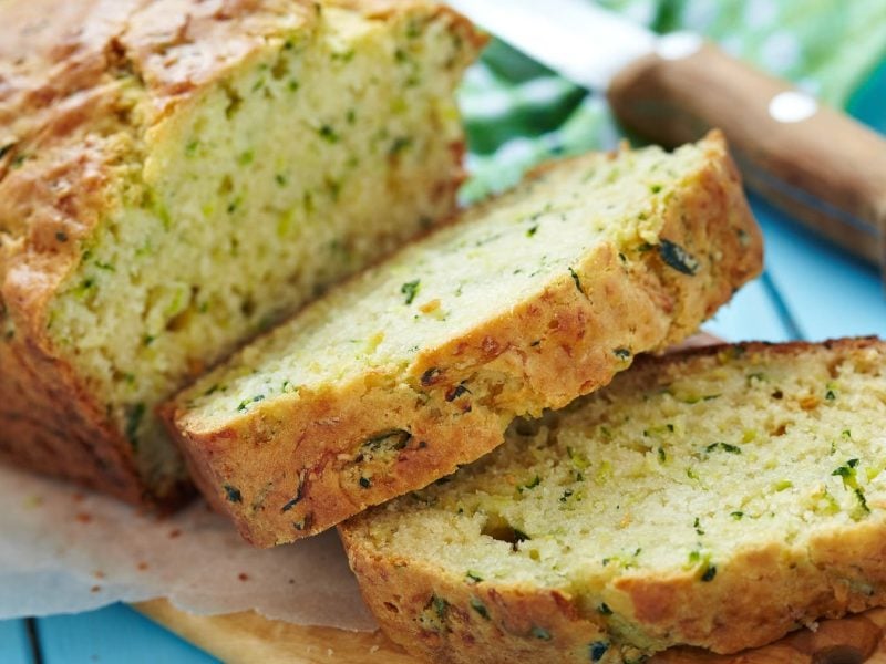 Das Zucchinibrot angeschnitten auf einem blauen Holztisch.