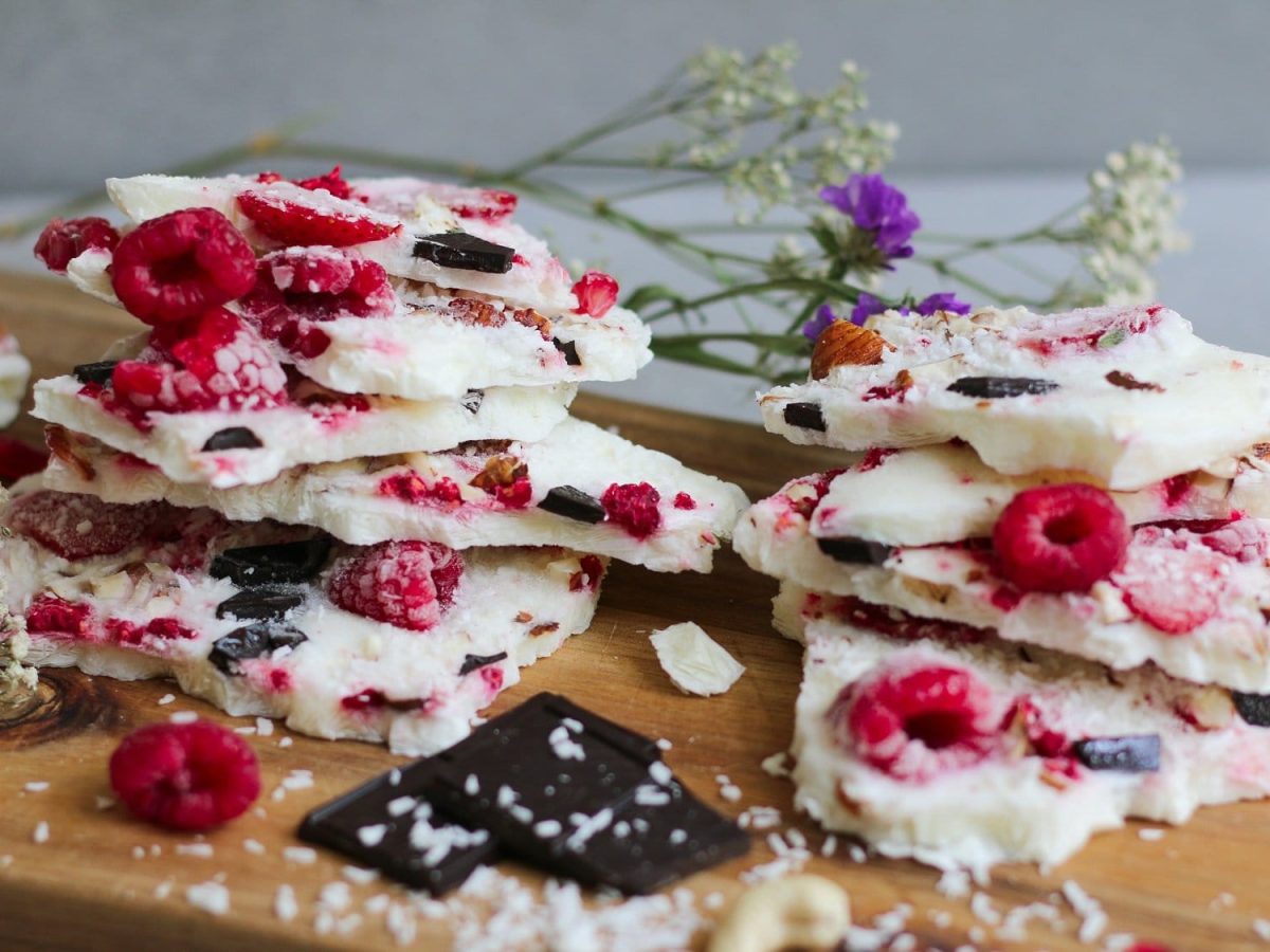 Ein paar Joghurt-Bites mit Beeren auf einem Brett gestapelt, im Hintergrund Blüten.