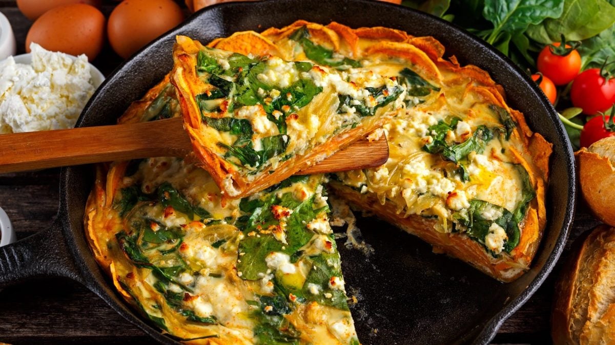 Eine schwarze Auflaufform mit der Kartoffel-Spinatquiche auf einem dunklen Holztisch.