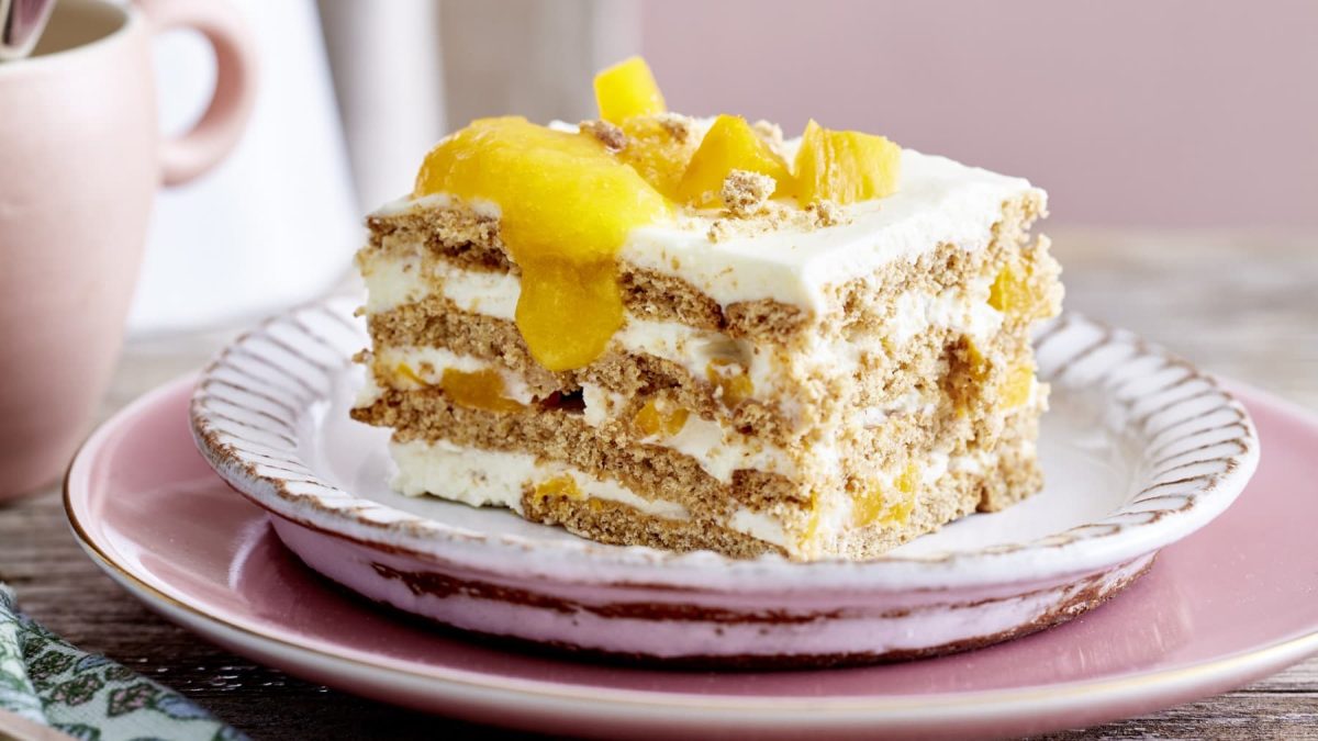 Eine Pfirsichschnitte auf einem weißen Dessertteller mit goldener Verzierung, auf einem rosa Teller, auf einem Holztisch.