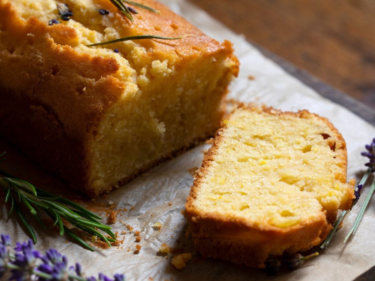 Ein angeschnittener Lavendelkuchen in Kastenform mit frischem Lavendel dekoriert.