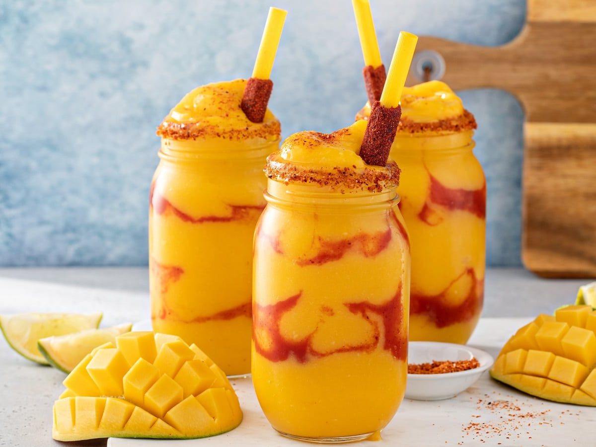 Drei Gläser mit Mangonada vor einem hellblauen Hintergrund.