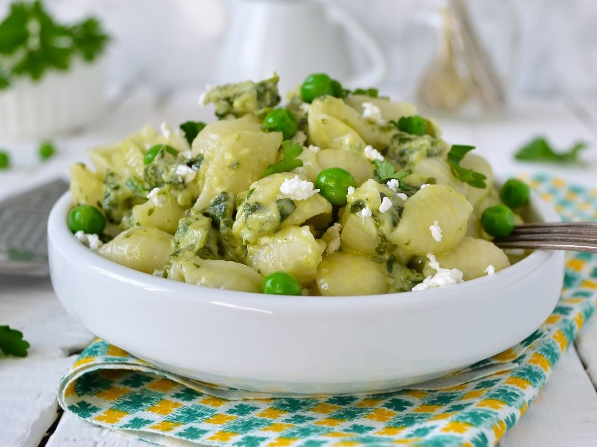 Ein tiefer Teller mit Nudelsalat mit Ricotta und Erbsen.