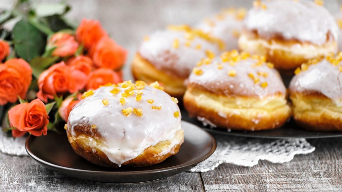 Pączki, polnische Krapfen, mit Zuckergus und getrockneten Früchten verziert, auf Tellern, im Hintergrund Rosen.