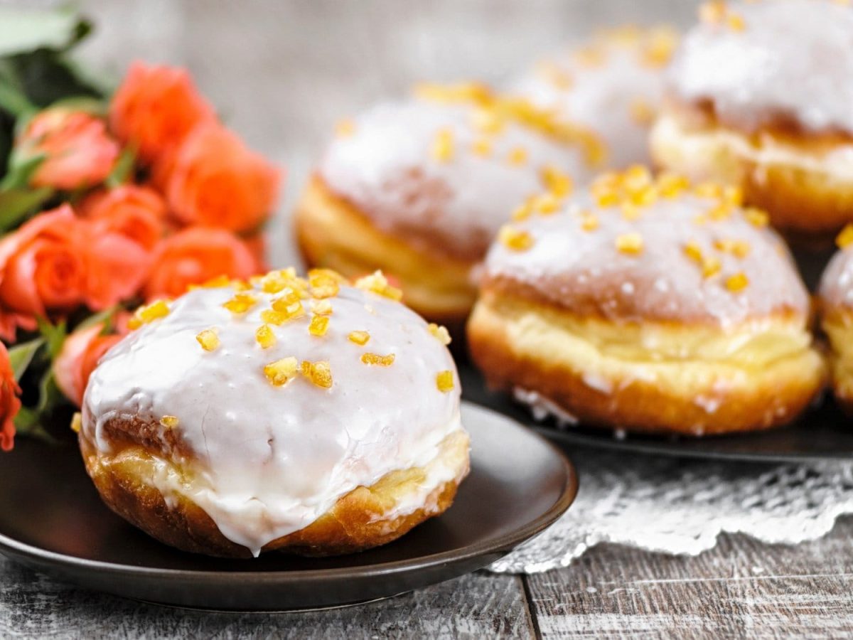 Pączki, polnische Krapfen, mit Zuckergus und getrockneten Früchten verziert, auf Tellern, im Hintergrund Rosen.