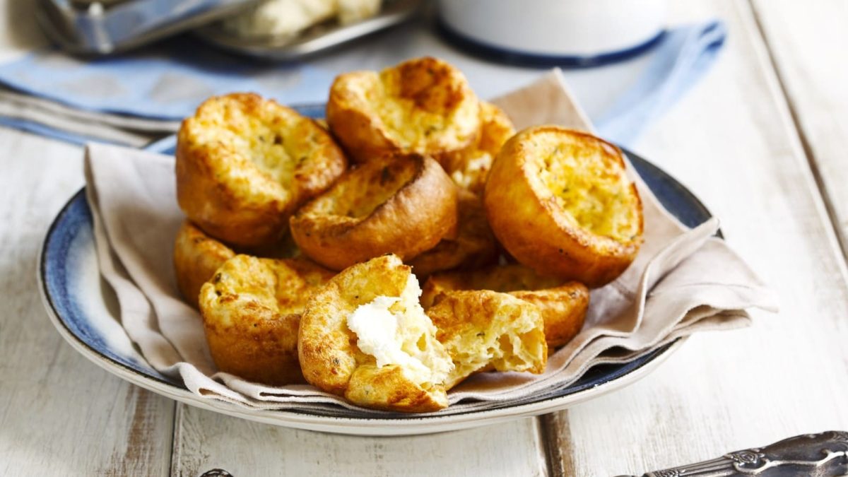 Ein Teller mit Parmesan Popovers auf einem weißen Holztisch.