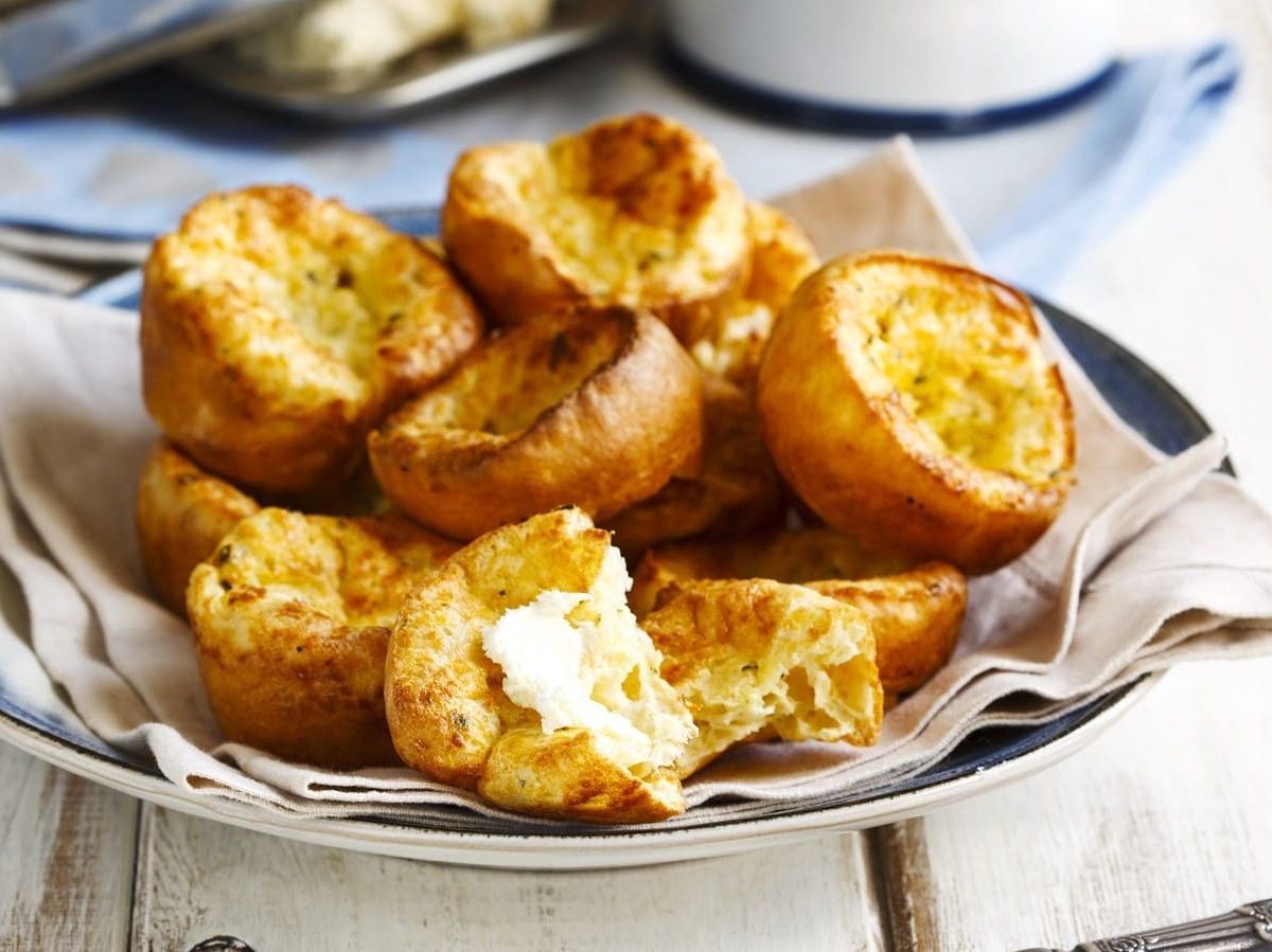 Ein Teller mit Parmesan Popovers auf einem weißen Holztisch.