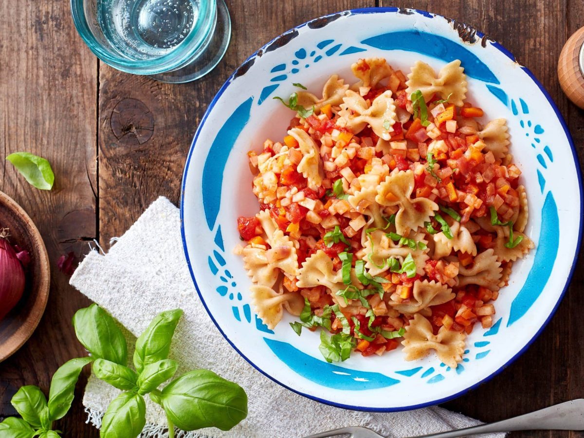 In einer Schüssel ist eine Portion Pasta mit Möhre und Sellerie angerichtet. Sie ist mit Basilikum verfeinert.