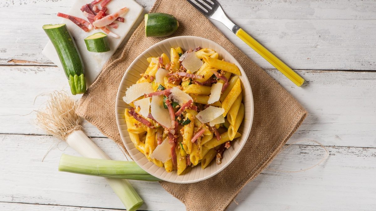 Ein tiefer Teller mit Penne mit Zucchini und Speck.