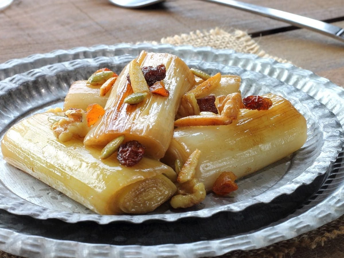 Ein Teller mit Porree mit Miso-Glaze und Nüssen auf einem Holztisch.