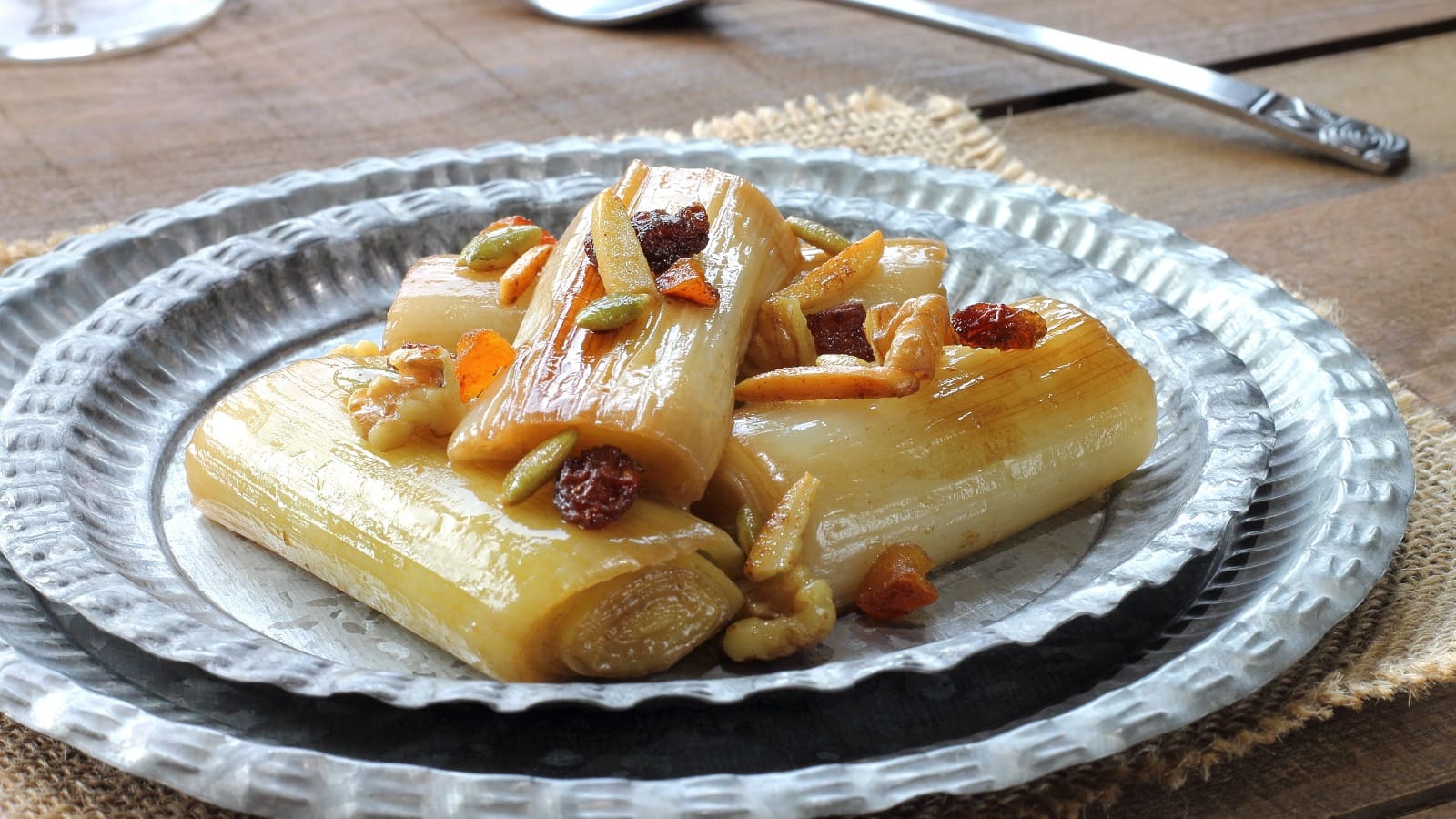 Ein Teller mit Porree mit Miso-Glaze und Nüssen auf einem Holztisch.