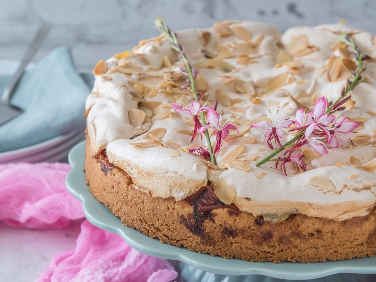 Der Rhabarber-Baiser-Kuchen auf einem hellblauen Tortenständer und grauem Steintisch. Daneben etwas pinker Tüll.