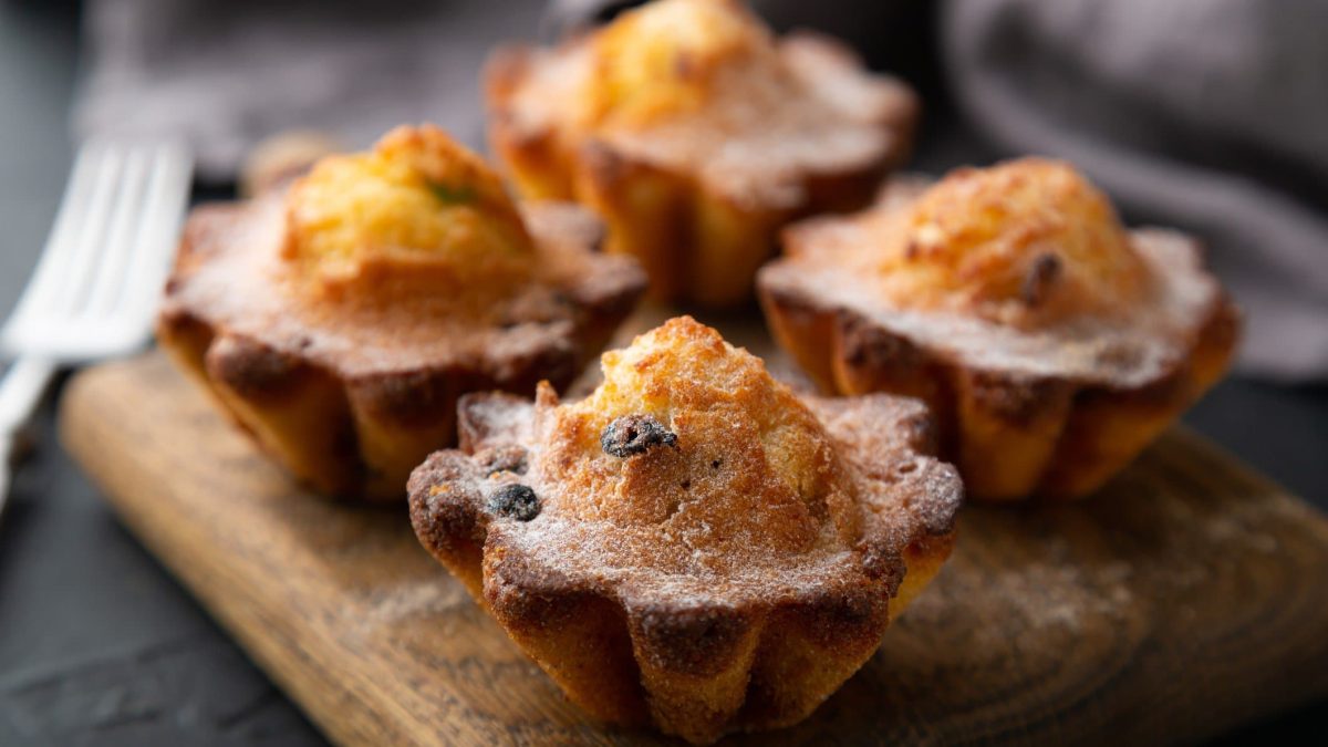 Vier Rosinen-Cupcakes mit Kokosmakronen auf Holzbrett und dunklem Untergrund. Draufsicht.