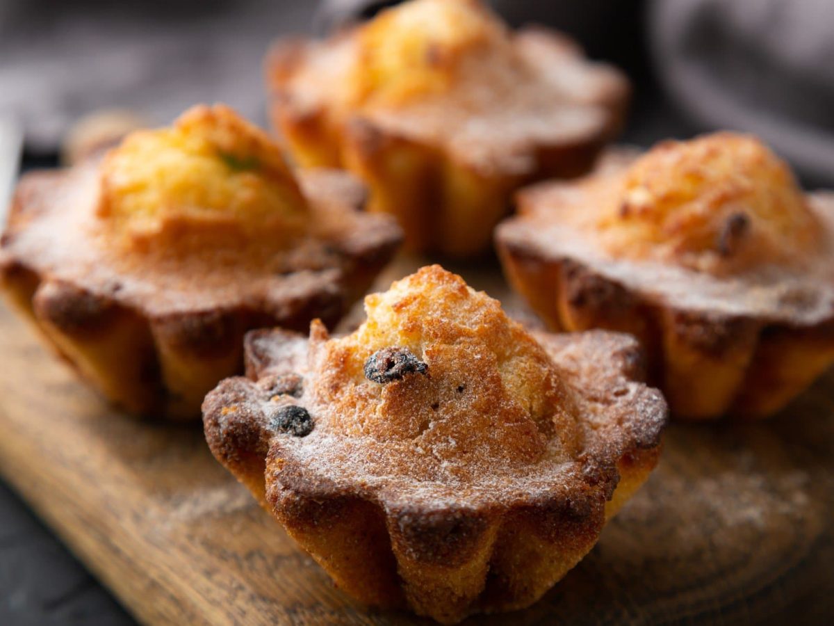 Vier Rosinen-Cupcakes mit Kokosmakronen auf Holzbrett und dunklem Untergrund. Draufsicht.